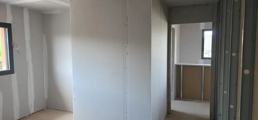Pose de plaques de plâtre sur ossature métallique en cours de chantier dans le Haut-Rhin, avec cloisons et rails visibles