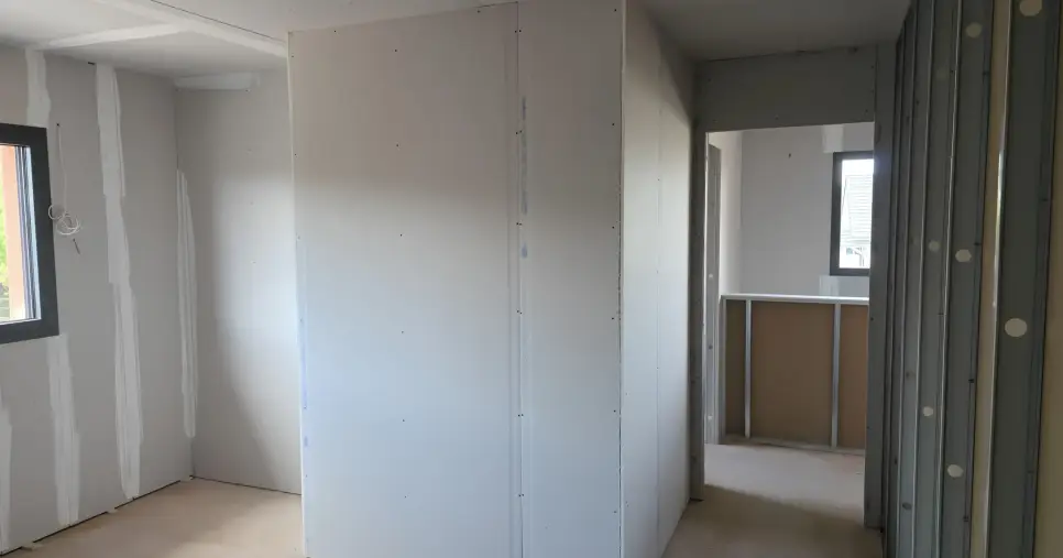 Pose de plaques de plâtre sur ossature métallique en cours de chantier dans le Haut-Rhin, avec cloisons et rails visibles